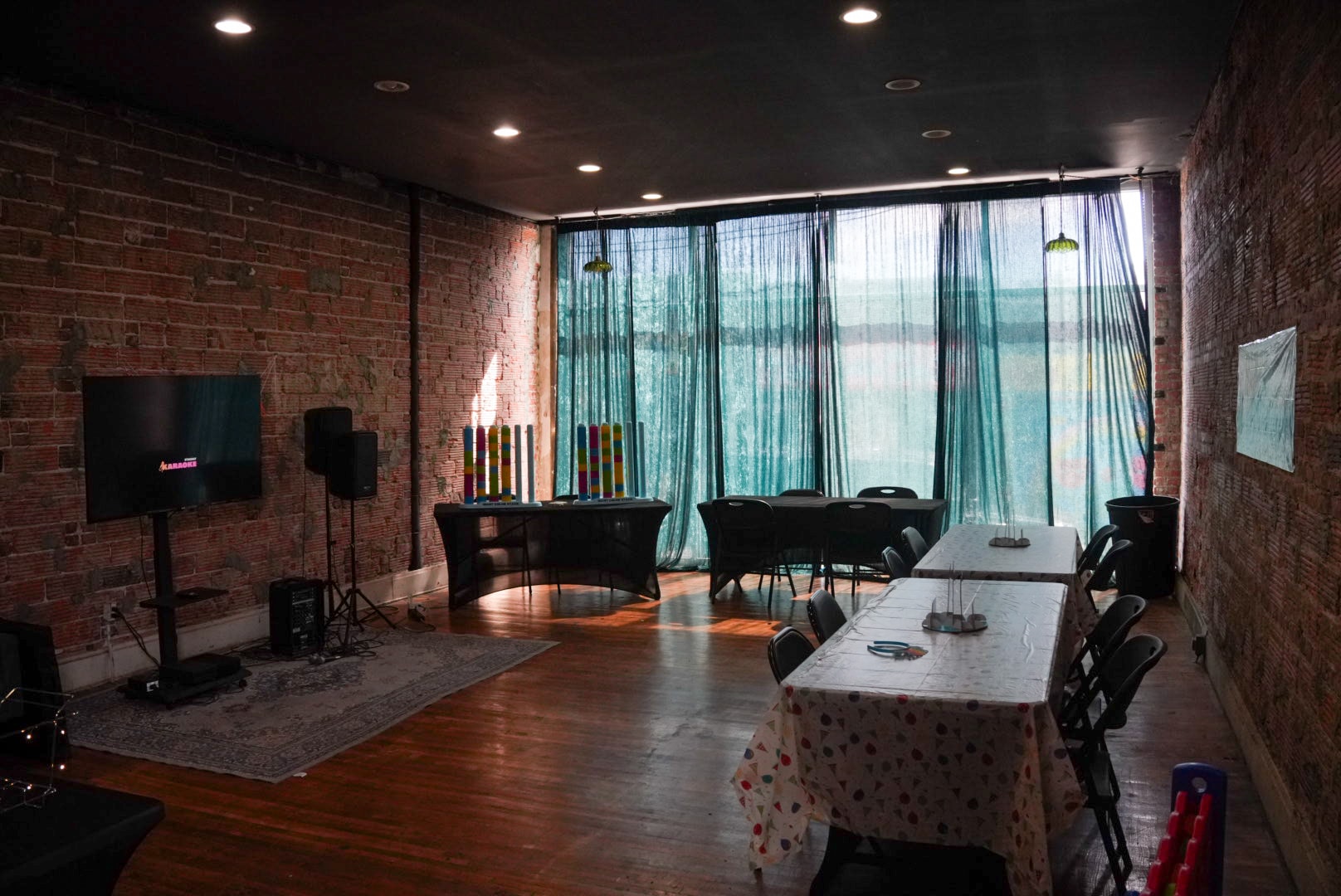 Event space with exposed brick, teal curtains, karaoke TV, and party tables