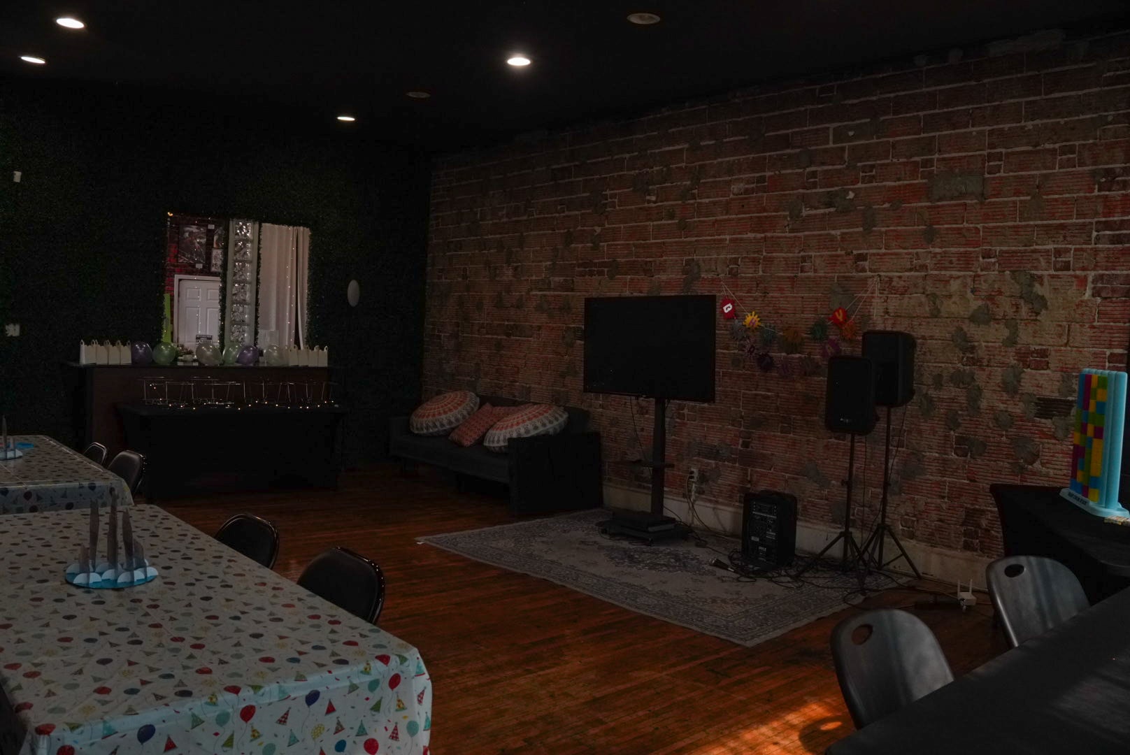 Event space interior with brick wall, TV screen, speakers, and lounge seating